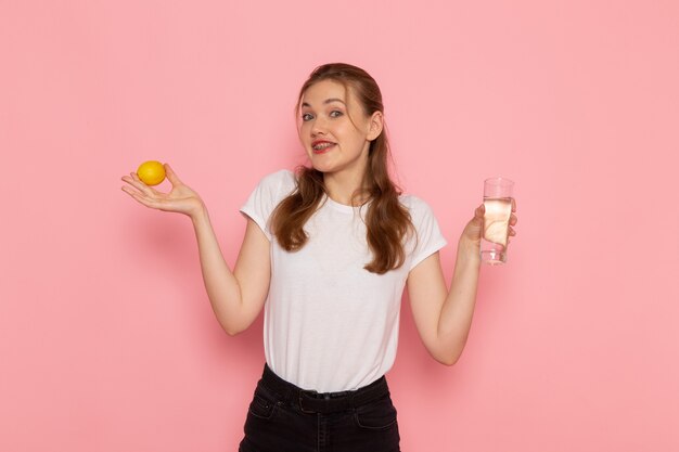 Front view of young female in white t-shirt holding fresh lemon and glass of water