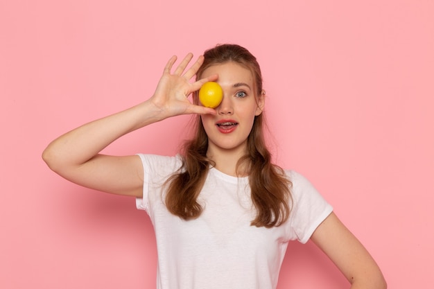 Free photo front view of young female in white t-shirt holding fresh lemon on the pink wall