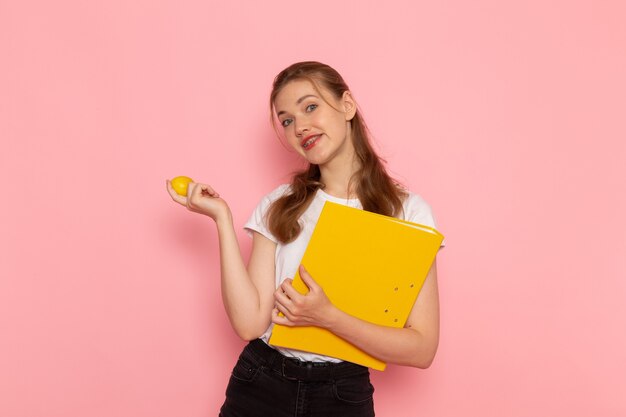 Вид спереди молодой женщины в белой футболке, держащей свежий лимон с файлами, улыбающейся на розовой стене