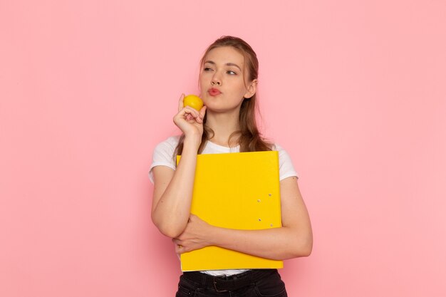 Front view of young female in white t-shirt holding fresh lemon with files thinking on pink wall