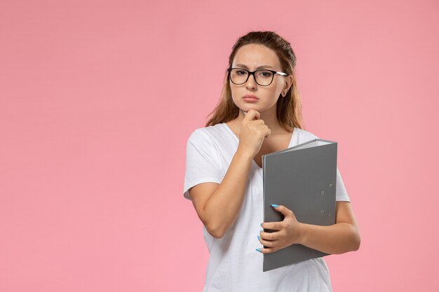 Front view young female in white t-shirt holding grey document with thinking expression on the pink background