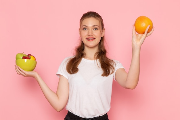 笑顔の新鮮な果物とプレートを保持している白いTシャツの若い女性の正面図