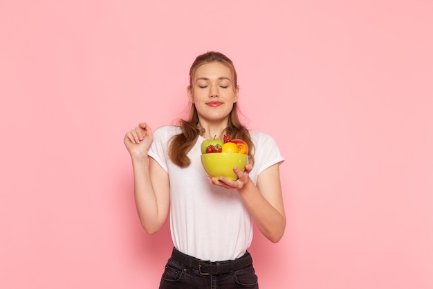 Front view of young female in white t-shirt holding plate with fresh fruits