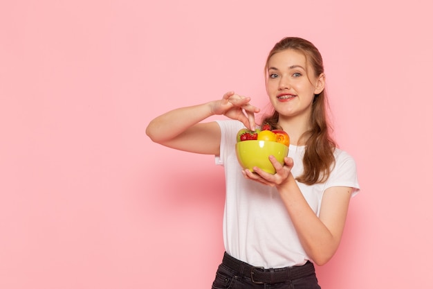 Front view of young female in white t-shirt holding plate with fresh fruits