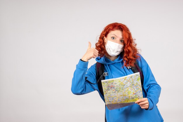 バックパックと白い壁の上のマスクの地図を持つ若い女性の正面図