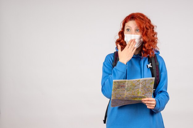 Front view of young female with backpack and map in mask on white wall