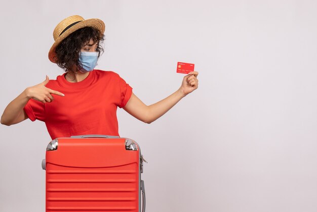 白い背景に赤い銀行カードを保持しているマスクの袋を持つ正面の若い女性 covid パンデミック休暇旅行観光客の色のお金