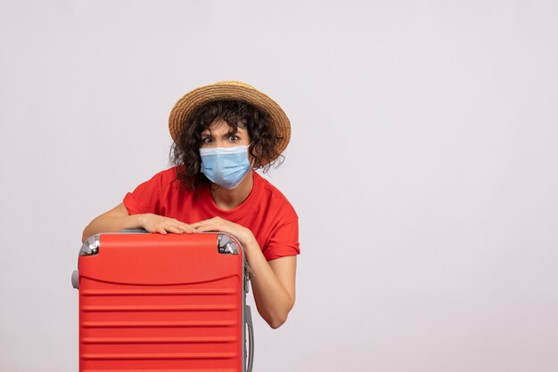 Вид спереди молодая женщина с сумкой в маске на белом фоне, цвет covid- путешествие, туристические каникулы, пандемия, солнечная поездка