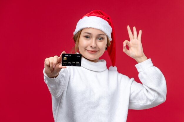 Вид спереди молодая женщина с банковской картой на красном фоне
