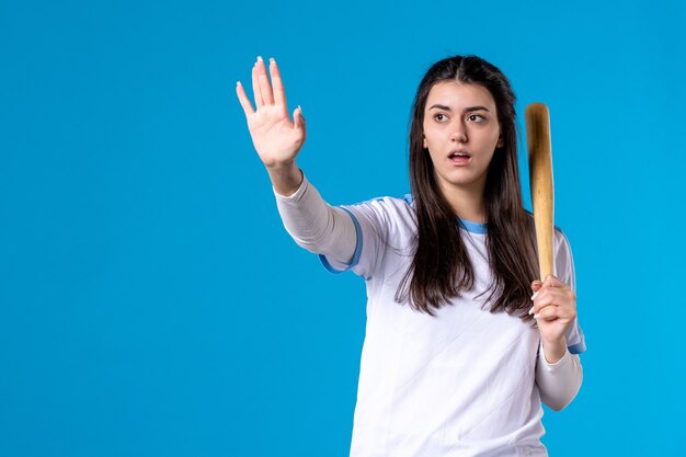 Вид спереди молодая женщина с бейсбольной битой на синей стене