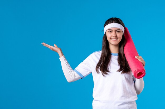 Front view young female with carpet for exercises on blue wall