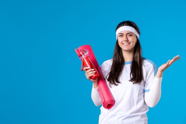 Front view young female with carpet for exercises and bottle of water on blue wall