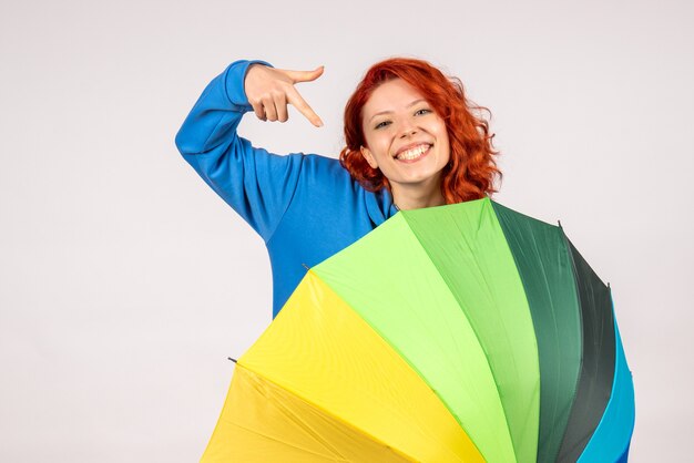 Front view of young female with colorful umbrella on the white wall