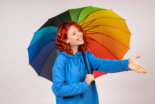 Front view of young female with colorful umbrella on white wall