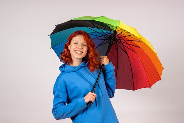 흰 벽에 화려한 우산을 가진 젊은 여자의 전면보기
