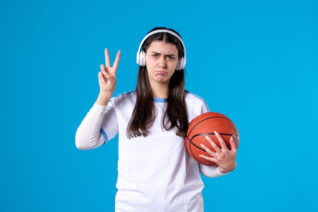 Front view young female with earphones holding basketball on blue wall
