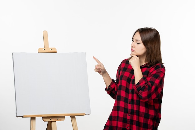 Free photo front view young female with easel for drawing on the white wall