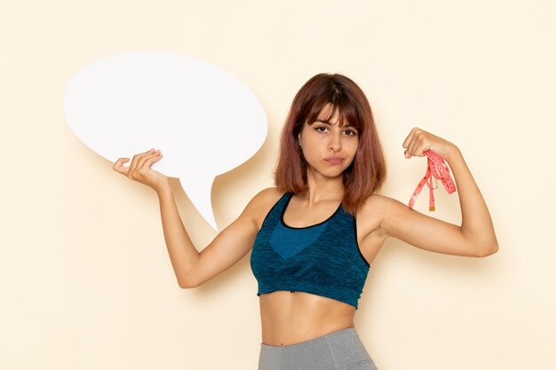 Front view of young female with fit body in blue shirt holding big white sign on white wall