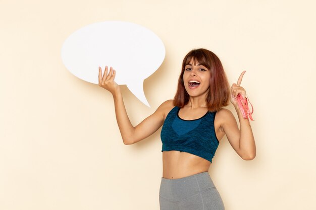Front view of young female with fit body in blue shirt holding huge white sign on light-white wall