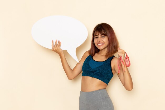 Front view of young female with fit body in blue shirt holding white sign on white wall