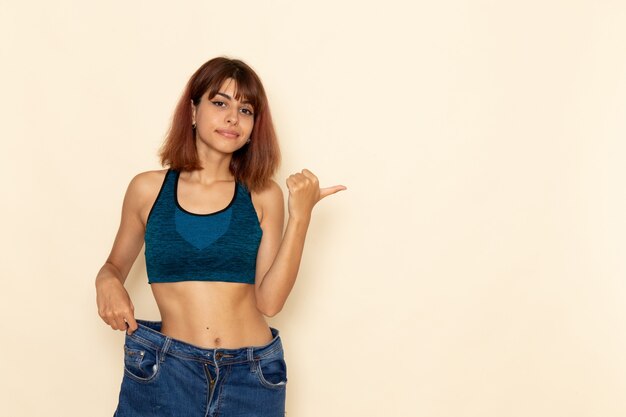 Front view of young female with fit body in blue shirt posing on the light white wall