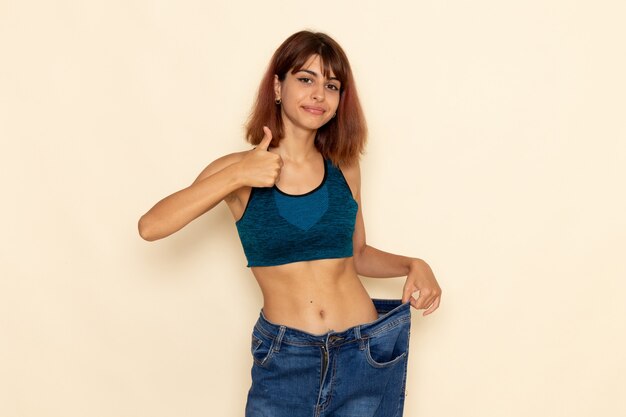 Front view of young female with fit body in blue shirt smiling on light-white wall