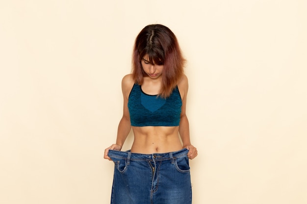 Front view of young female with fit body in blue shirt on the white wall