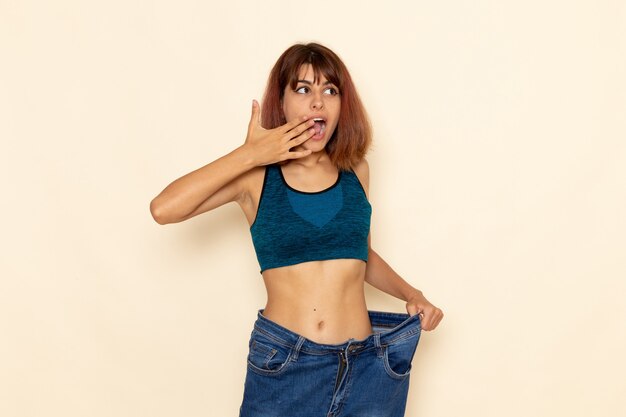 Front view of young female with fit body in blue shirt on white wall