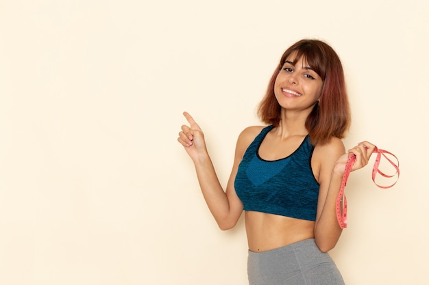 Vista frontale di giovane donna con corpo in forma in camicia blu con sorriso sul muro bianco chiaro