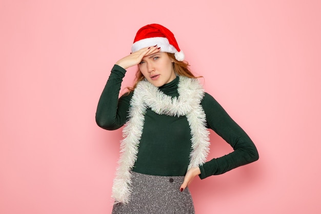 Front view of young female with garlands in red cap stressed on pink wall