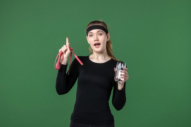 Front view young female with glass of water and waist measure on green background sport athlete woman workout body color black