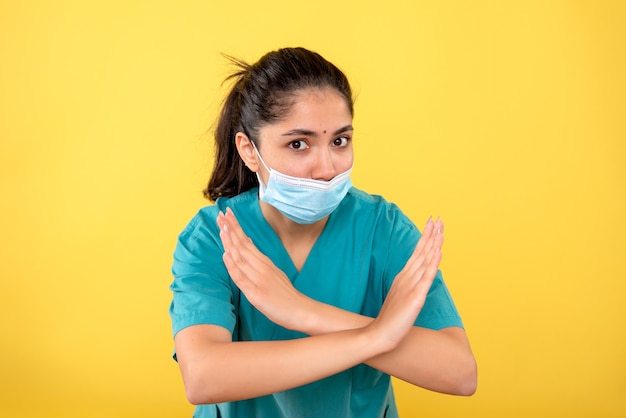 Front view of young female with medical mask crossing hands on yellow wall