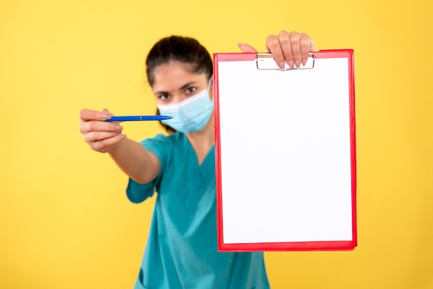 Free photo front view of young female with medical mask holding clipboard on yellow wall