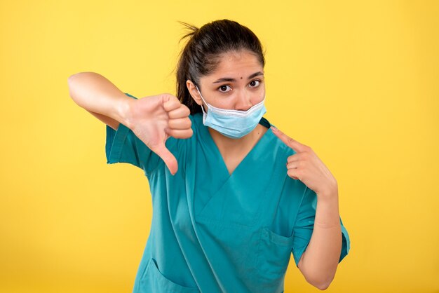 Front view of young female with medical mask making thum down sign on yellow wall