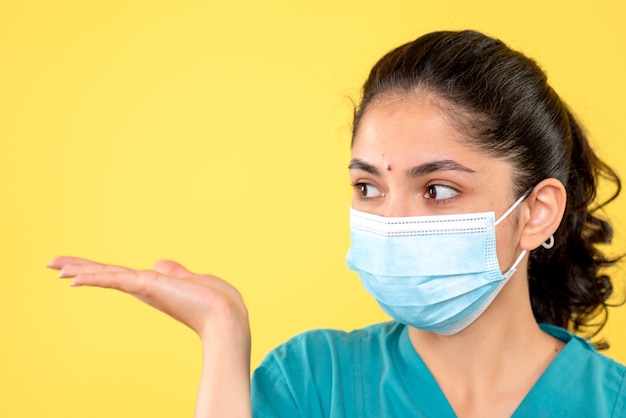 Front view of young female with medical mask on yellow isolated wall