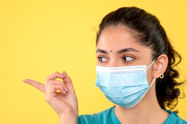 Front view of young female with medical mask on yellow wall