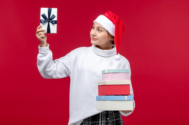 Вид спереди молодая женщина с новогодними подарками на светло-красном фоне