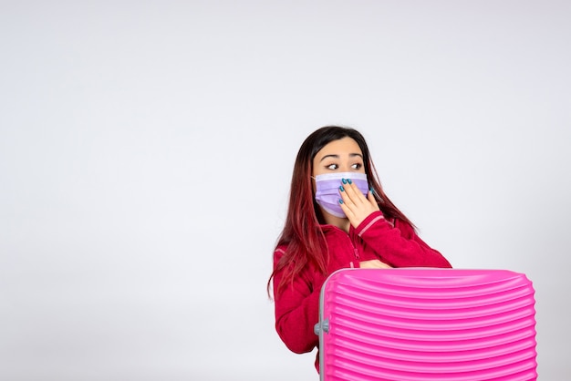 Vista frontale giovane femmina con borsa rosa in maschera sul muro bianco pandemia virus donna vacanza covid- viaggio di colore