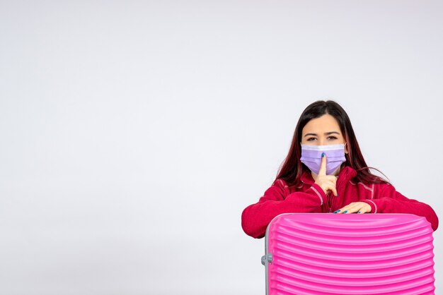 Front view young female with pink bag in mask on white wall vacation pandemic virus covid- color trip woman