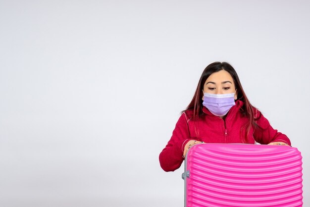 Vista frontale giovane femmina con borsa rosa in maschera sul muro bianco virus donna vacanza covid viaggio di colore