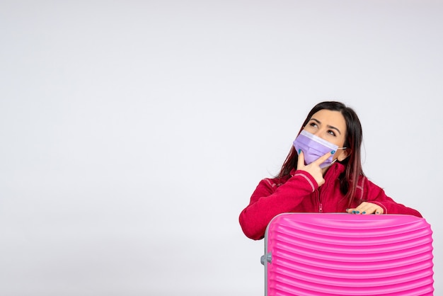 Front view young female with pink bag in sterile mask thinking on the white wall virus vacation covid color pandemic trip woman