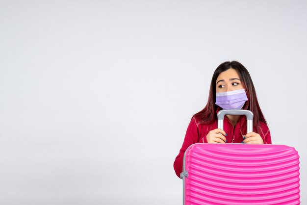 Вид спереди молодая женщина с розовой сумкой в стерильной маске на белой стене, цветная вирусная женщина, отпуск с пандемией