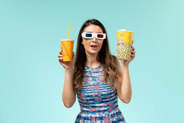 밝은 파란색 표면에 d 선글라스에 팝콘 패키지와 음료 전면보기 젊은 여성