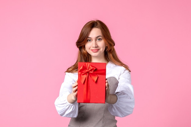 Вид спереди молодая женщина с подарком в красной упаковке на розовом фоне свидание любви марш горизонтальный подарок духи равенство женщина фото деньги