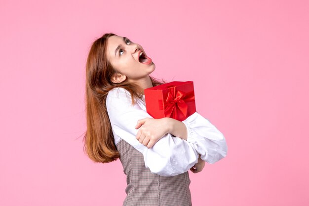 Front view young female with present in red package on pink background love date march horizontal sensual equality woman