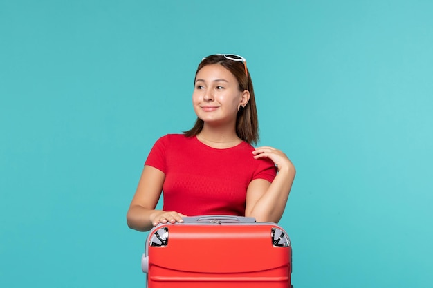 Giovane femmina di vista frontale con la borsa rossa che si prepara per le vacanze sullo spazio azzurro