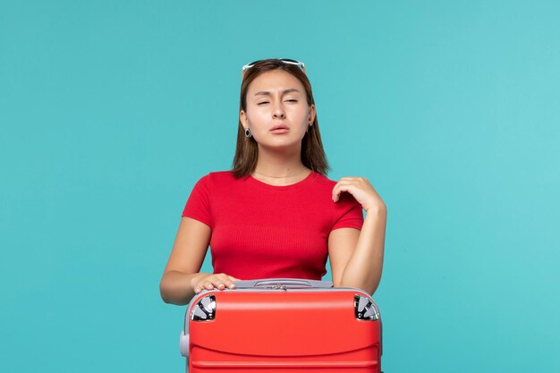 正面図水色の空間で休暇の準備をしている赤いバッグを持つ若い女性