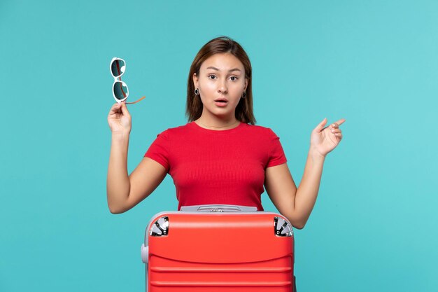 Free photo front view young female with red bag holding her sunglasses on light-blue space