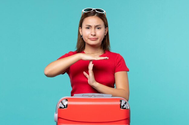 青いスペースで休暇の準備をしている赤いバッグを持つ若い女性の正面図