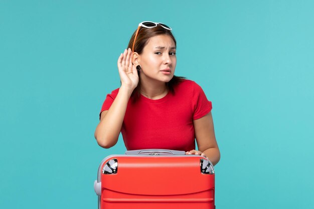 Front view young female with red bag preparing for vacation trying to hear on blue space